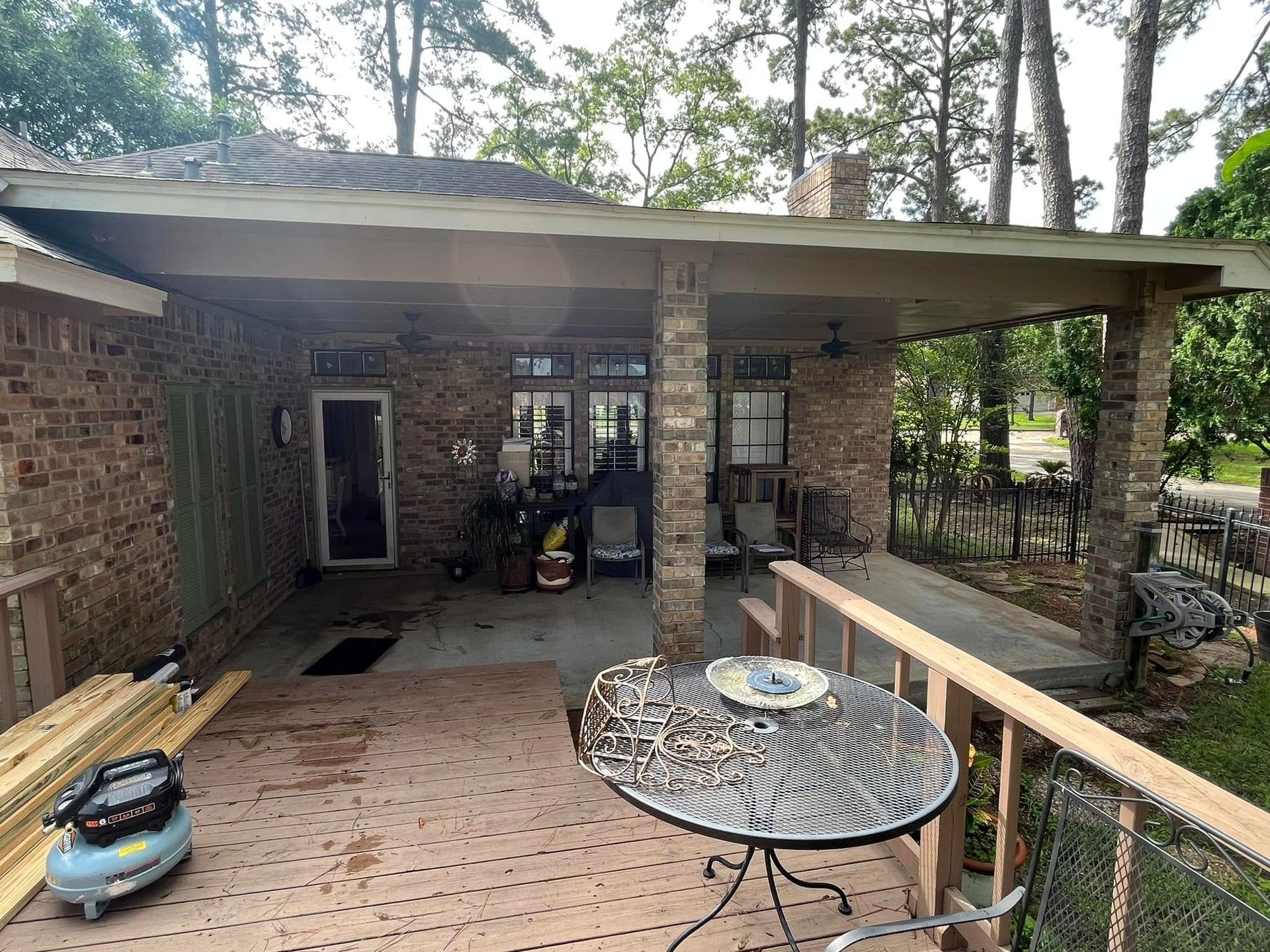 Covered brick porch with outdoor furniture, a table, and wooded yard beyond.