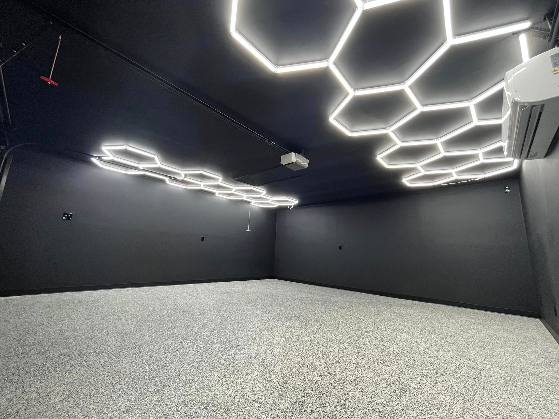 Empty dark room with black walls, gray carpet, and glowing hexagonal ceiling lights