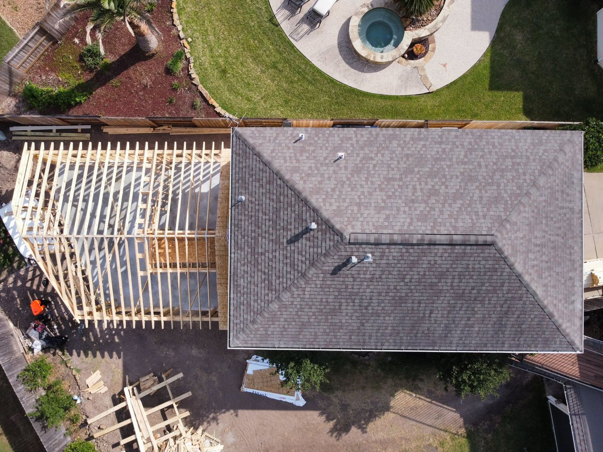 Aerial view of a house roof with a wooden deck frame, lawn, and circular patio area.