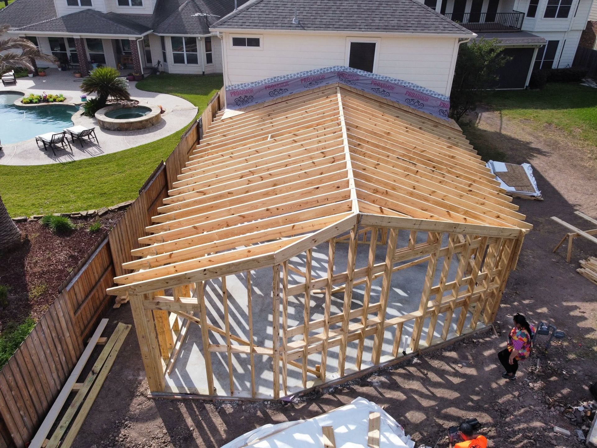 Partially framed house addition with exposed wood beams in a suburban backyard, two people nearby