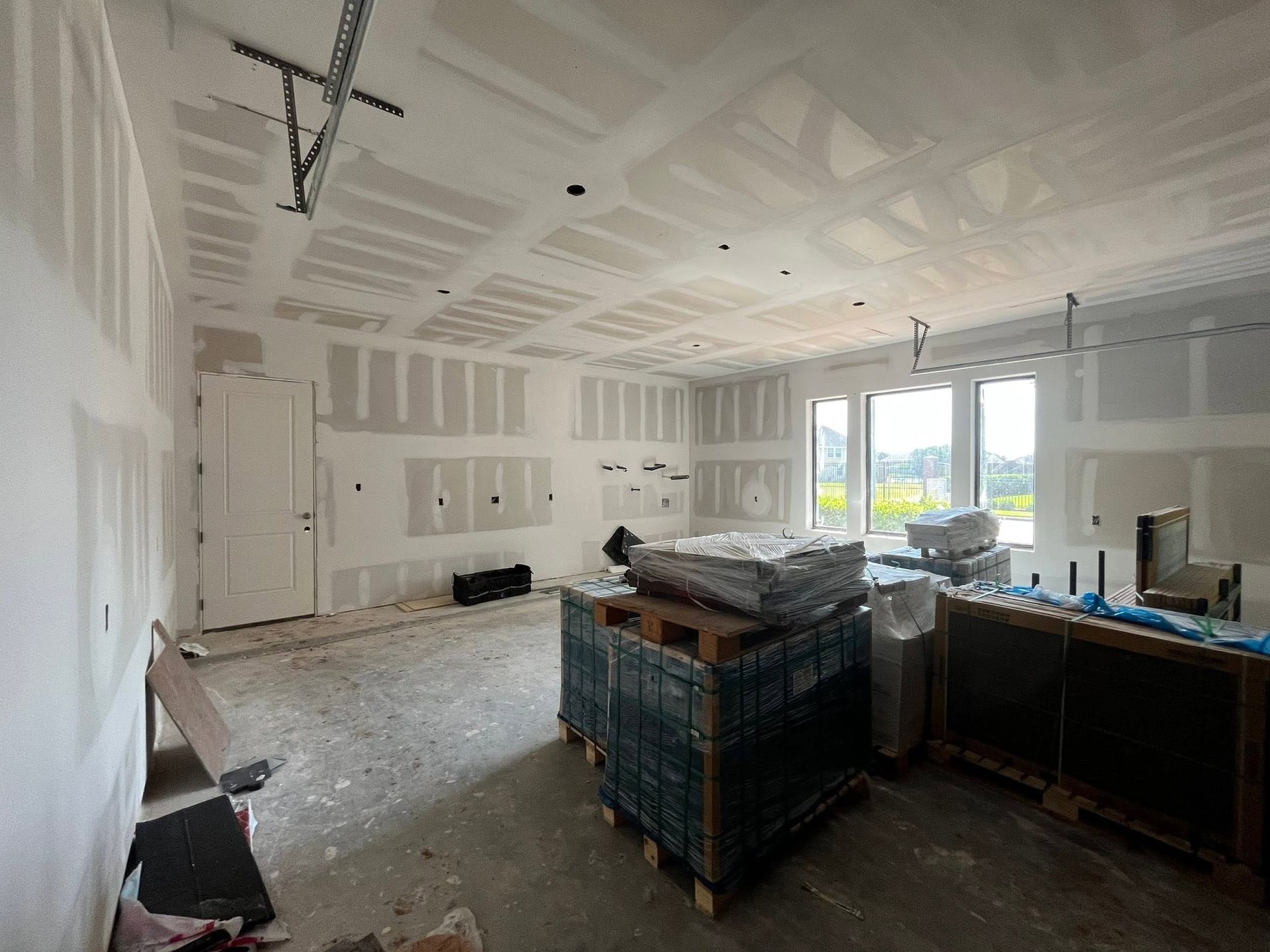 Unfinished room with drywall, exposed ceiling, construction debris, and large windows letting in daylight