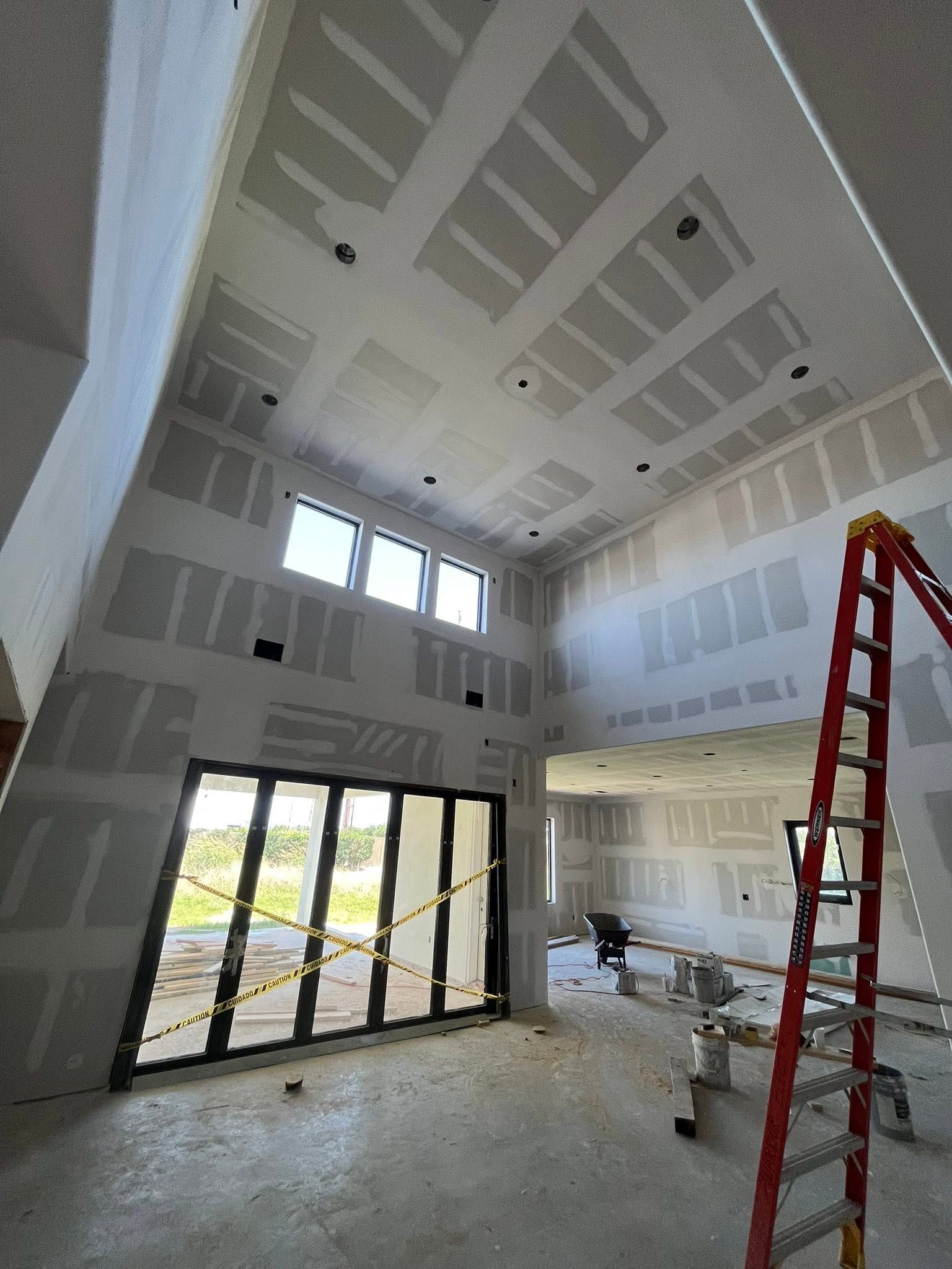 Unfinished interior with high vaulted ceiling, large windows, drywall, and a red ladder on the floor.