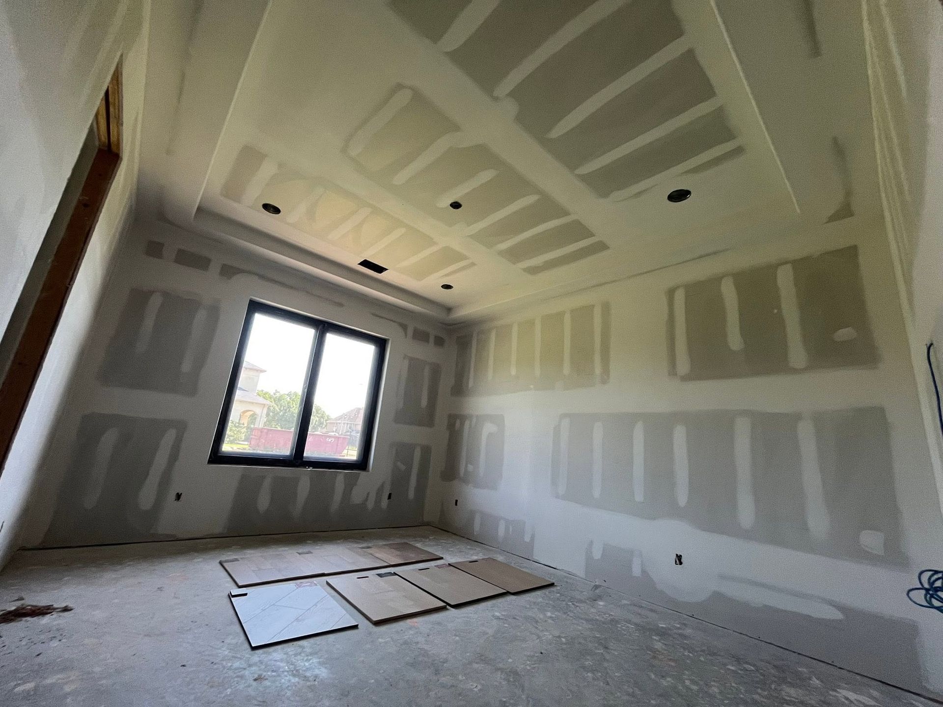 Empty drywall room with taped seams, recessed ceiling, and a window letting in daylight.