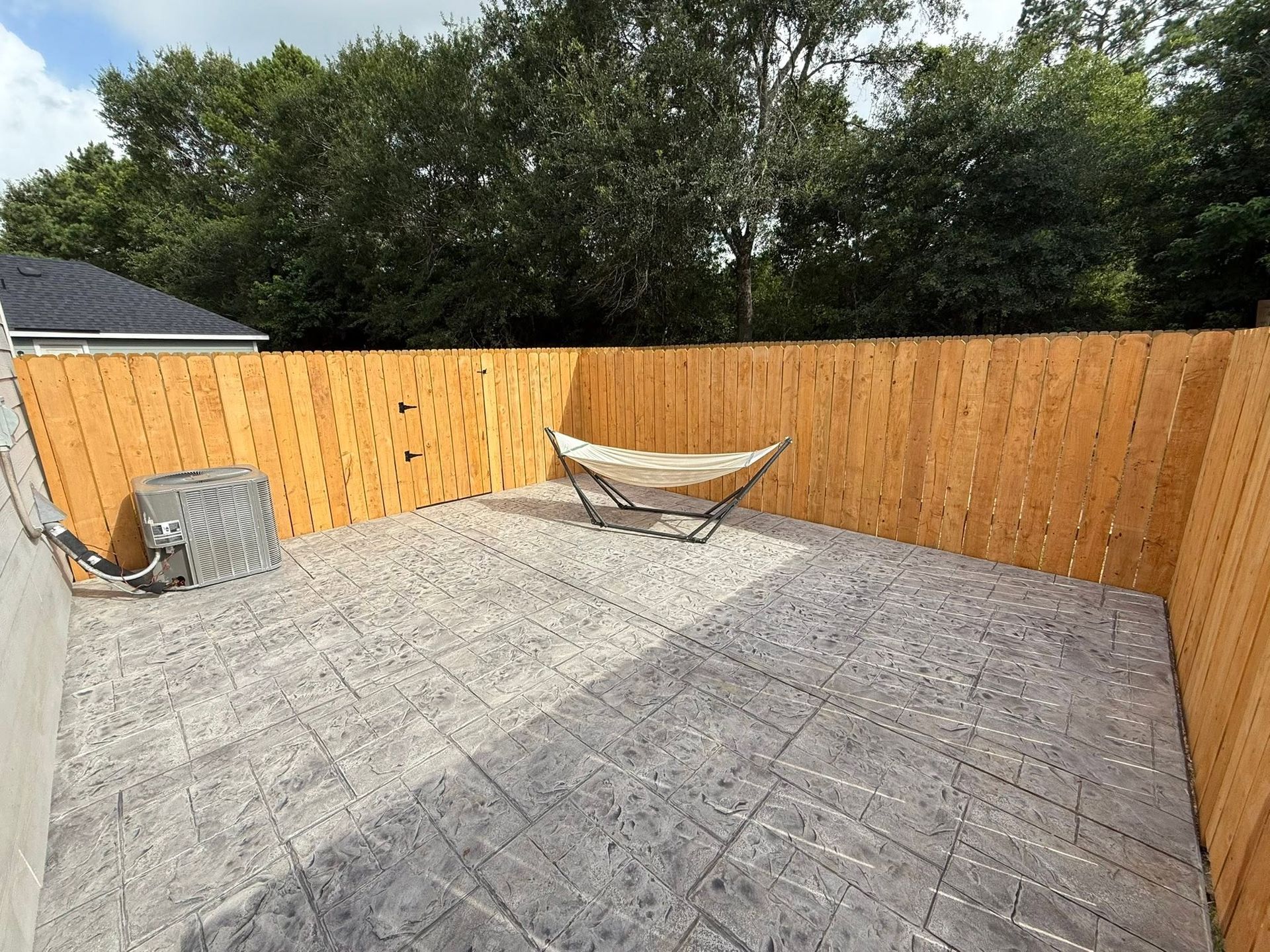 Backyard patio with gray pavers, wooden fence, trees, and a hammock in the corner