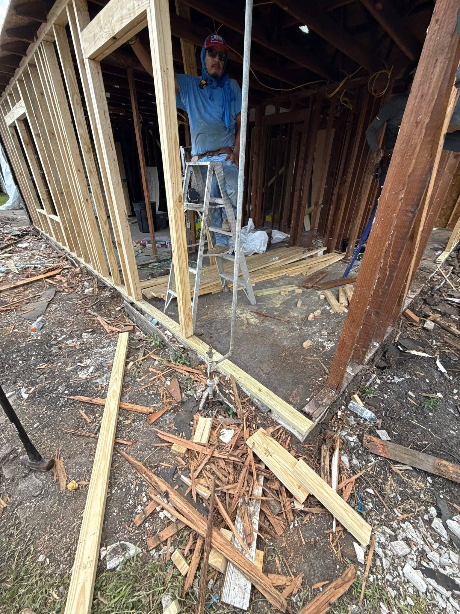 Worker inside a damaged, stripped room with exposed studs and debris on the floor