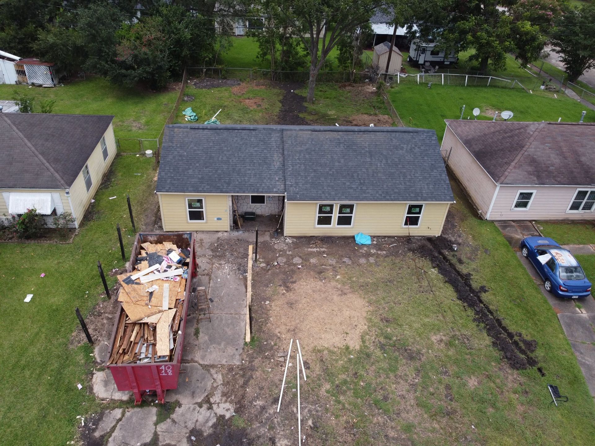 Aerial view of a backyard with a beige house, red dumpster, and a large dirt lot enclosed by fences.