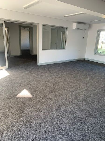 A Large Empty Room With A Gray Carpet And White Walls — Flooring Direct Mid North Coast in South Kempsey, NSW