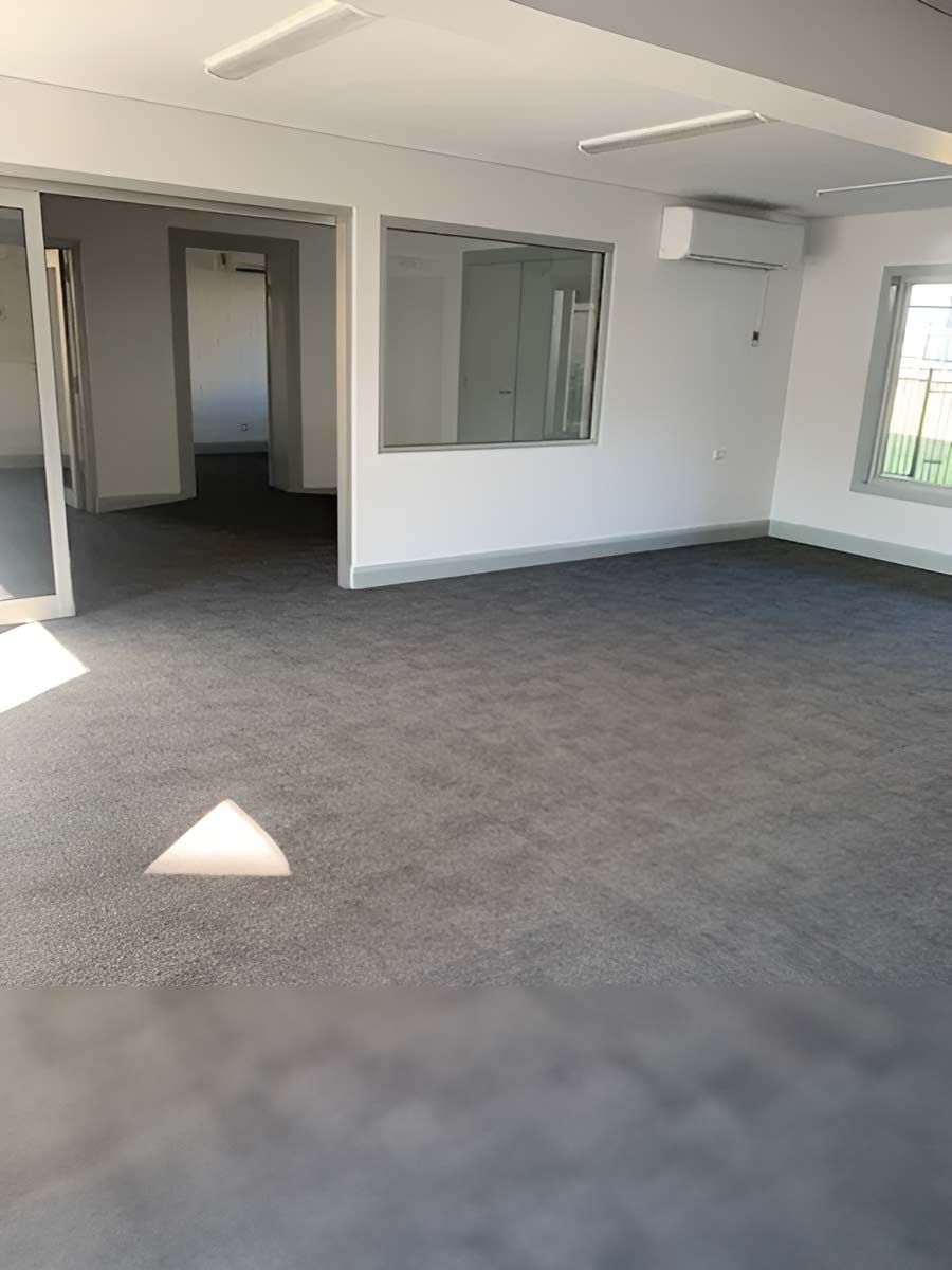 A Large Empty Room With A Gray Carpet And White Walls — Flooring Direct Mid North Coast in South Kempsey, NSW