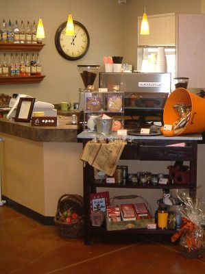 Coffee shop counter with espresso machine, wall clock, shelves, and pastries displayed by the register