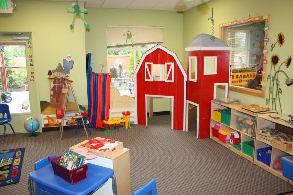 Colorful preschool classroom with a red play barn, toys, books, and child-sized furniture
