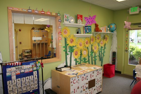 Colorful classroom corner with sunflower wall art, alphabet cards, a calendar, and a mirror near a door and window