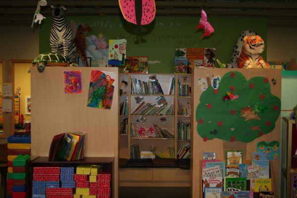 Colorful classroom shelves with books, posters, and a green paper tree display under stuffed animals on a wall