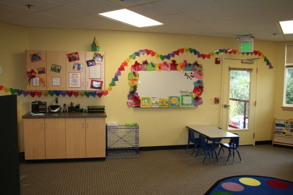 Colorful classroom with cabinets, wall art, small table and chairs, and a doorway to the outside.