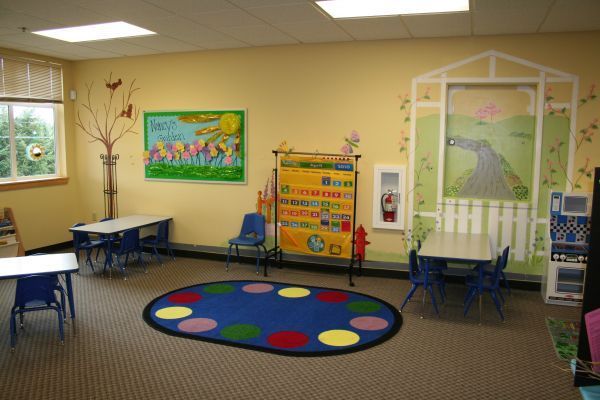 Classroom reading nook with small tables, blue chairs, colorful rug, and wall art