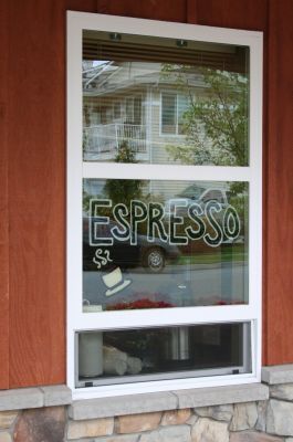 Storefront window with “ESPRESSO” sign in white on black, framed by red siding and stone base