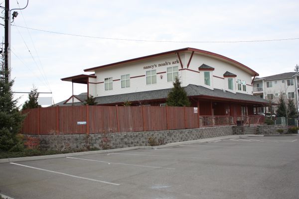 Large white building with red roof behind a wooden fence on a quiet street.