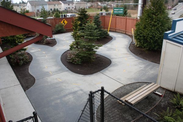 Empty courtyard with curved concrete paths, small trees, and a chain-link fence under overcast skies