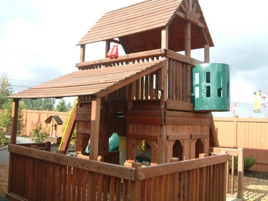 Wooden backyard playhouse with a slide and elevated tower inside a fenced play area