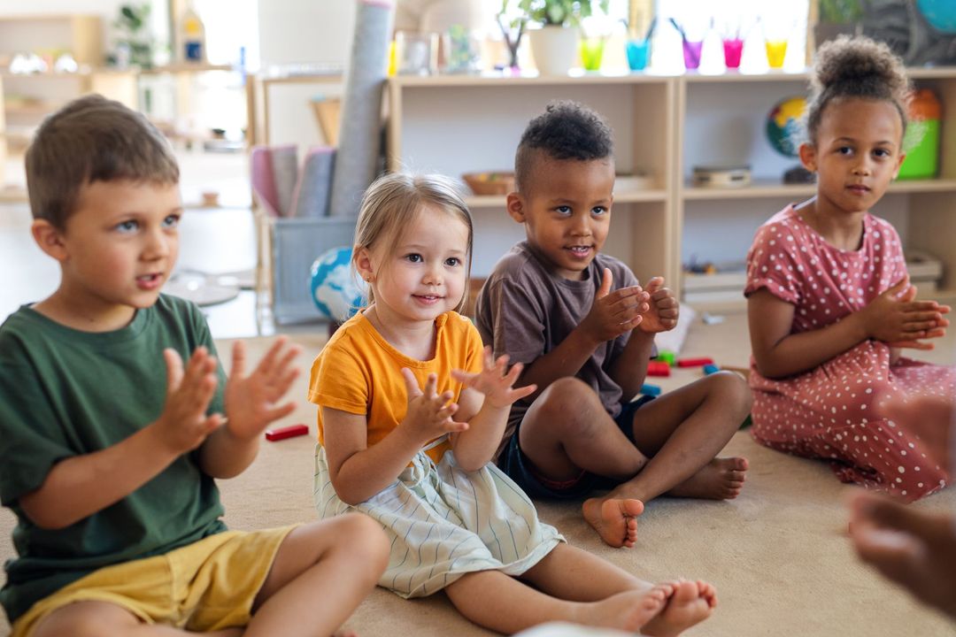 Children sitting on a classroom carpet and clapping during a group activity