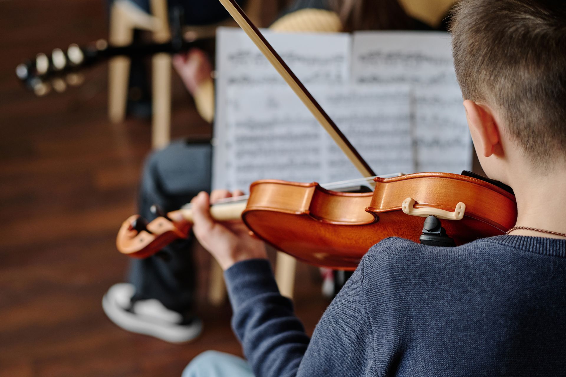 Child playing violin in a music lesson, with sheet music and a teacher nearby