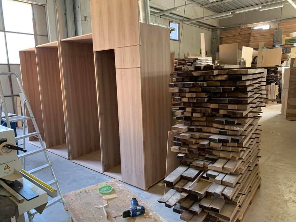 Strutture di armadi in legno al naturale in lavorazione nel laboratorio, con tavole e componenti di legno impilati sullo sfondo