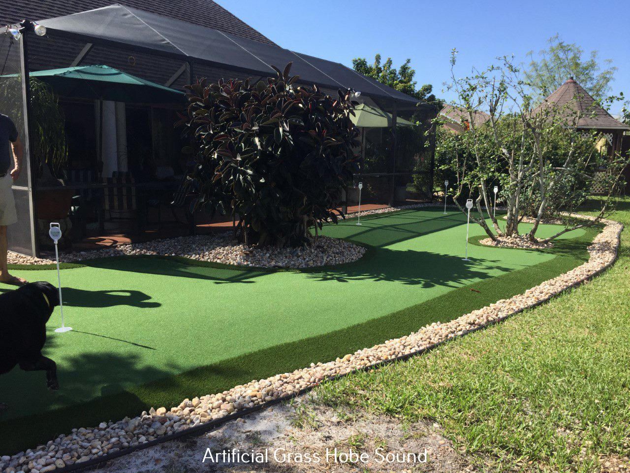 Backyard with artificial turf putting green bordered by rocks and landscaping.