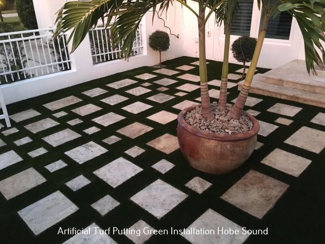 Patio with alternating squares of artificial turf and stone, potted palm tree.