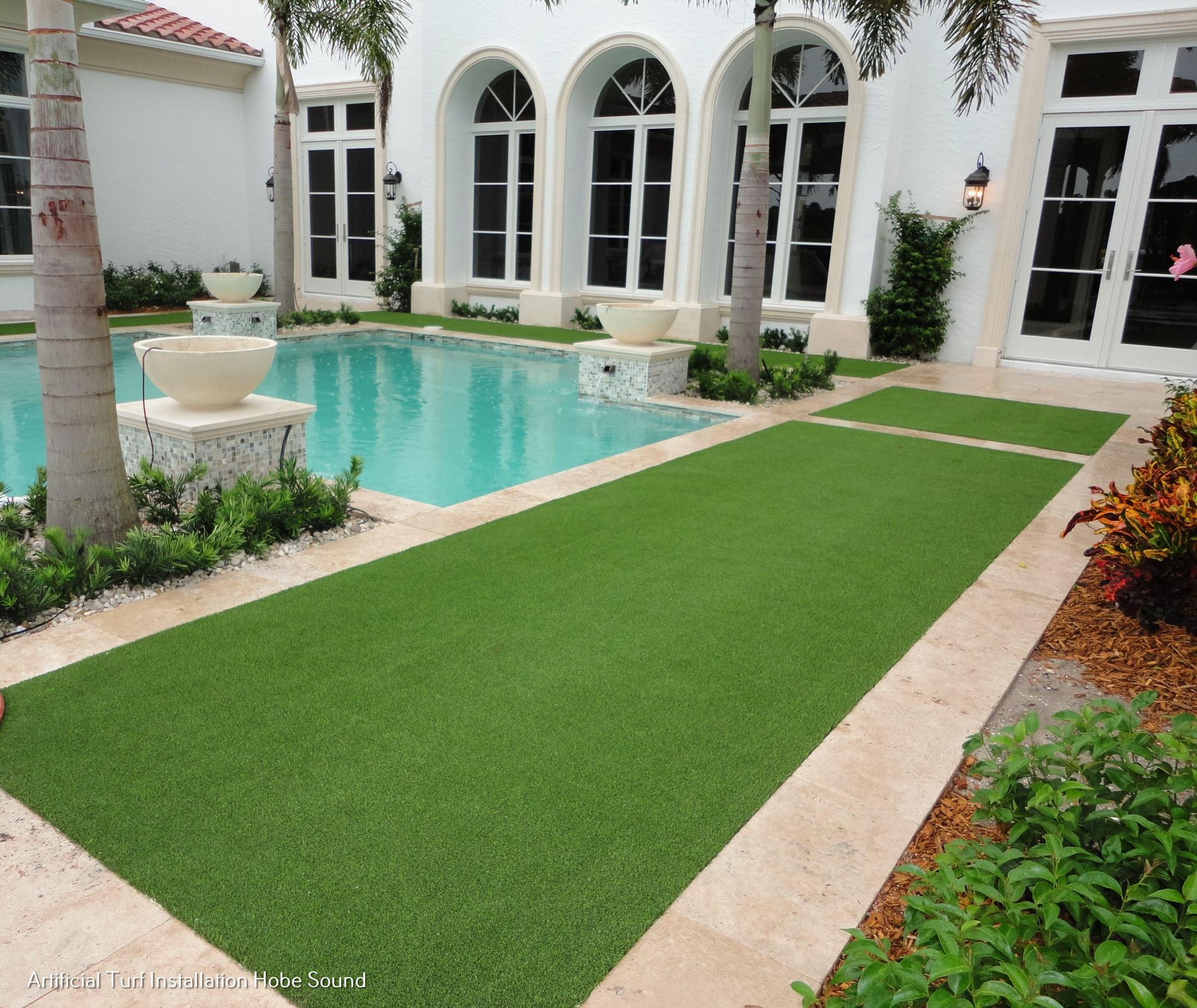 Artificial turf pathway next to a pool in a courtyard with white arches.