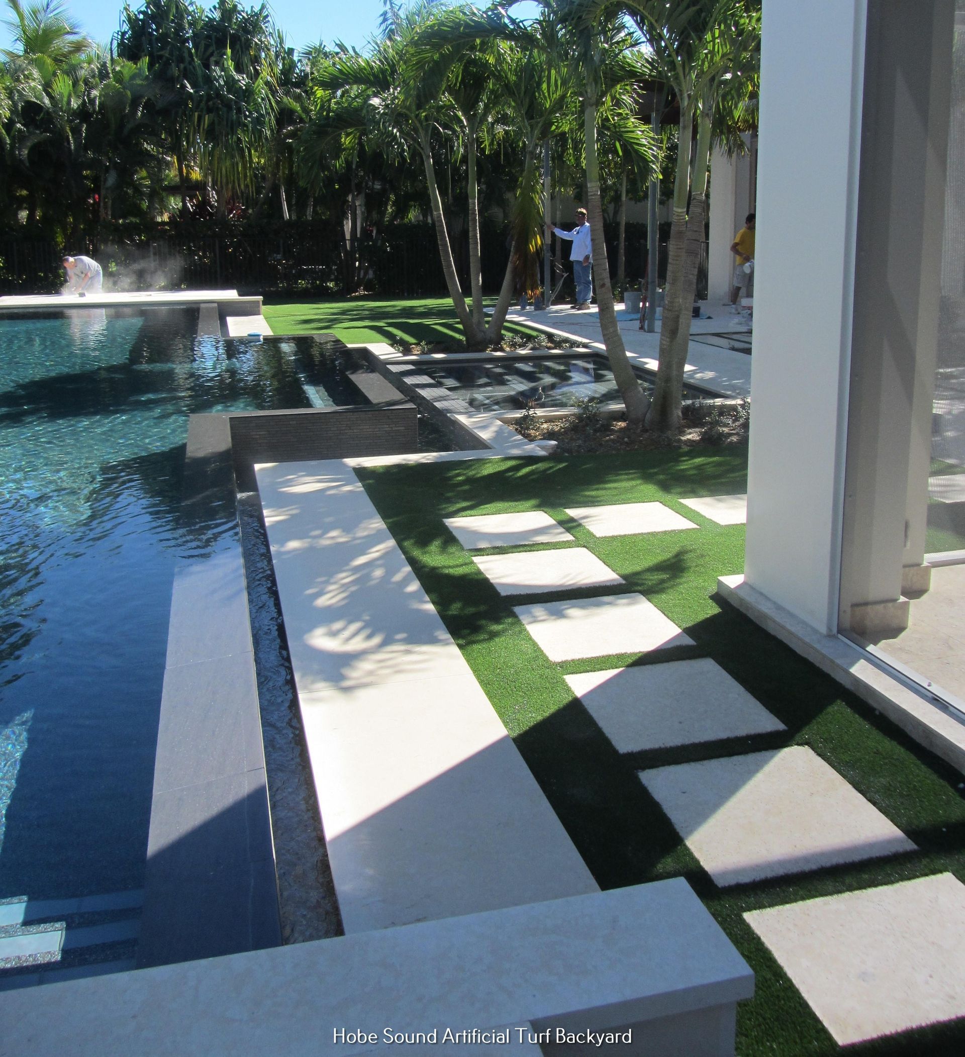 Poolside landscape with a pool, concrete paths, artificial turf, and palm trees.