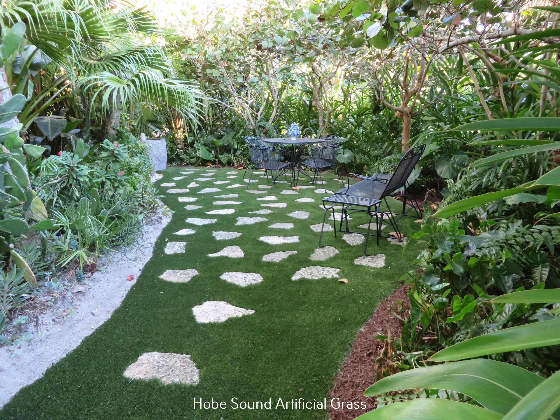 A lush garden with a stepping-stone path, artificial grass, and patio furniture.
