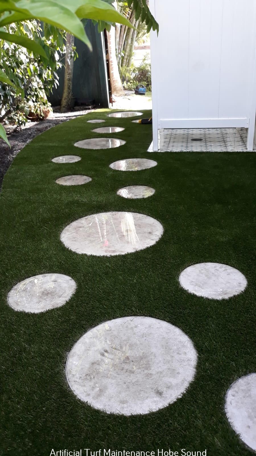Circular stepping stones on green turf leading towards a white building.
