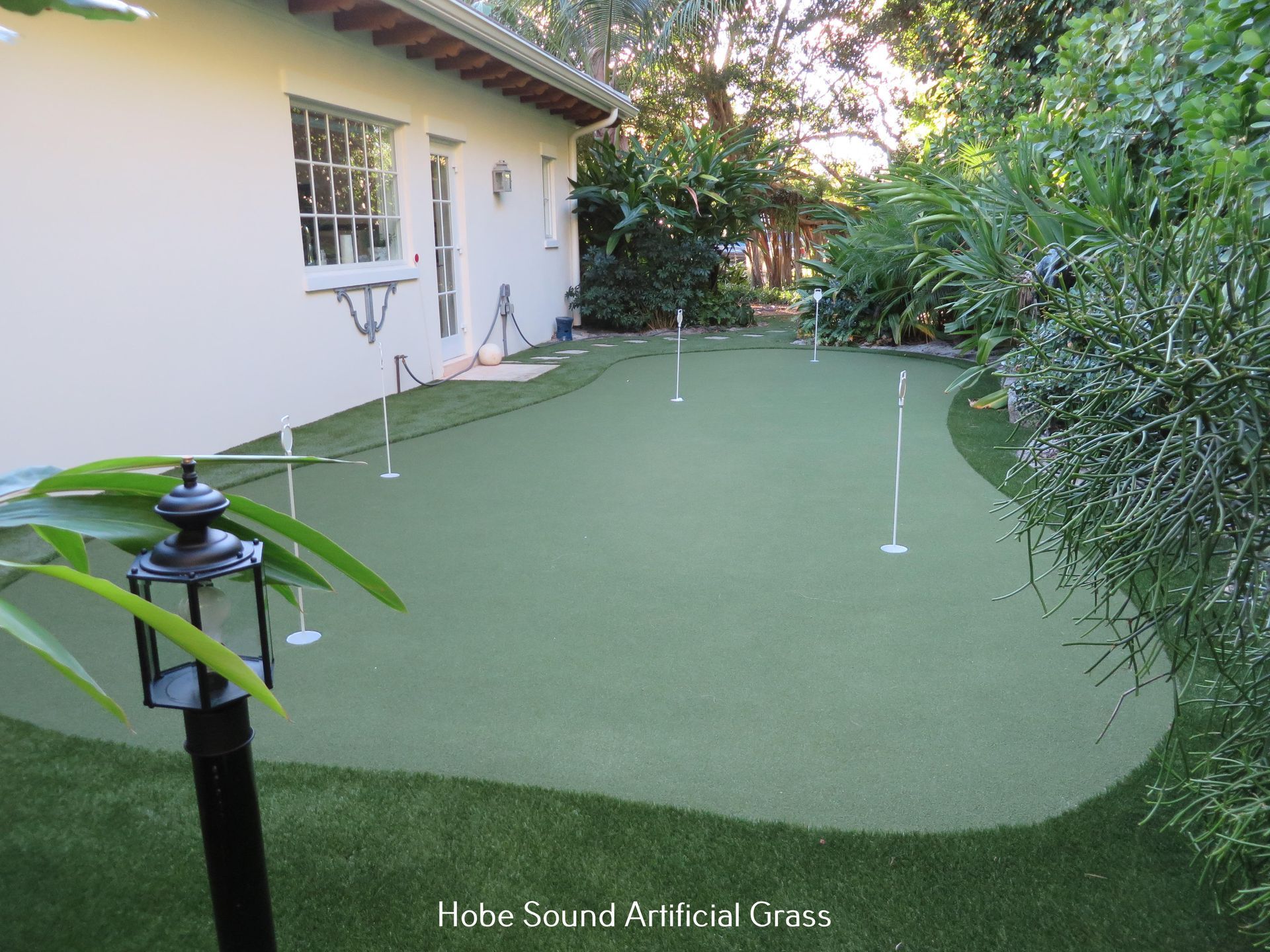 A putting green made of artificial turf in a backyard setting near a house.