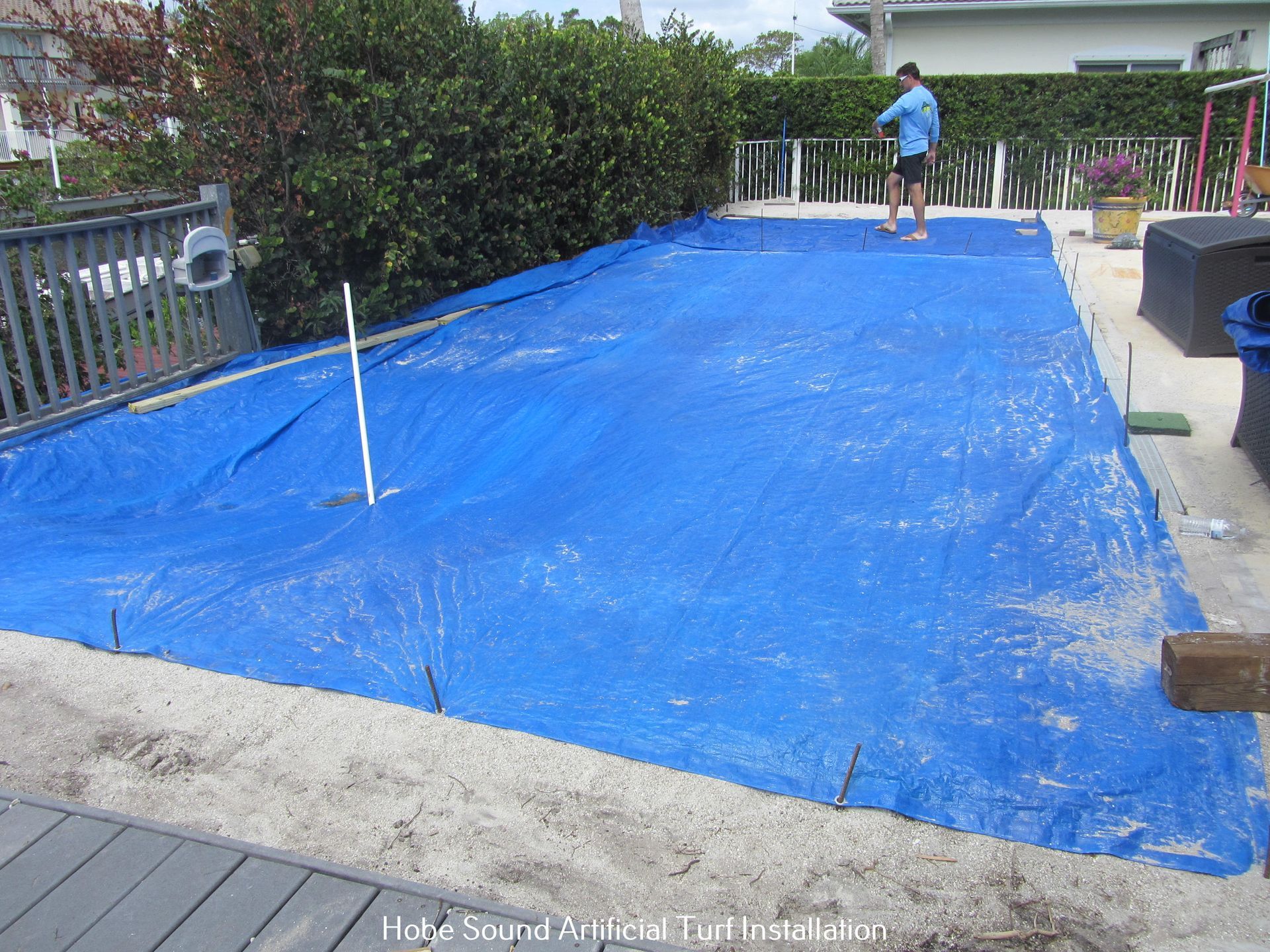 Blue tarp covers pool; person stands nearby. Concrete patio and shrubbery are visible.