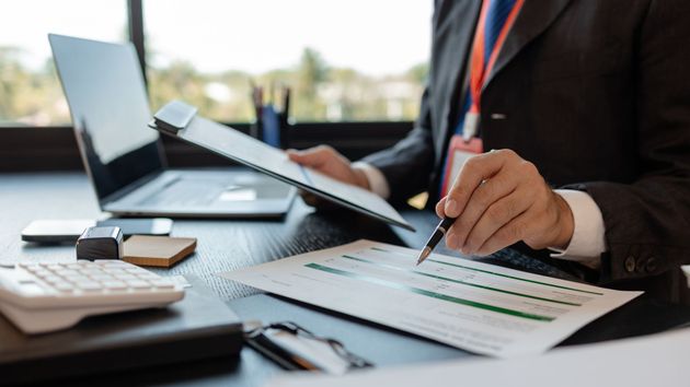 Person reviewing documents at a desk with laptop, calculator, and pen in an office setting