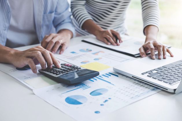 Hands using a calculator and laptop over printed financial charts on a desk