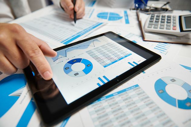 Hands using a tablet over business charts and graphs on a desk with calculator and papers