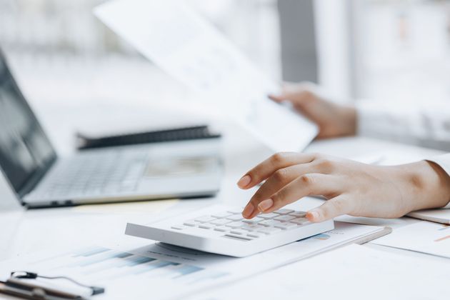 Hands using a calculator beside a laptop on a desk with financial documents