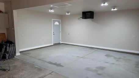 Empty garage with gray floor, white walls, overhead lights, and a door.