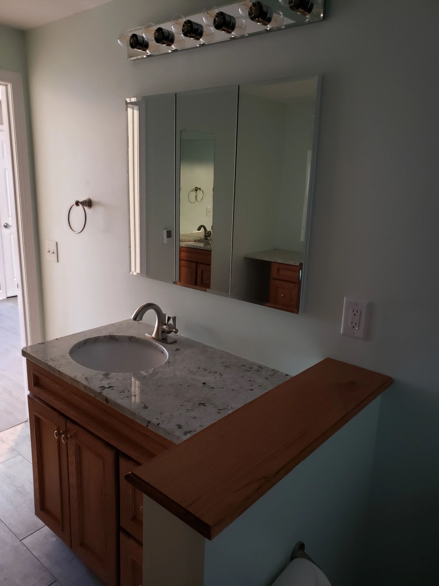 Bathroom with vanity, mirror, and light fixture; light blue walls, wood cabinetry, and a granite countertop.