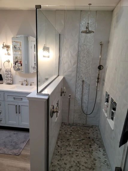 Bathroom with glass shower, pebble floor, and white walls. Vanity with mirror and storage.