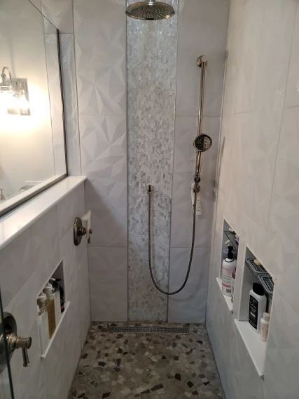 Shower with white geometric tile, recessed shelves, and pebble floor. Silver shower head and fixtures.