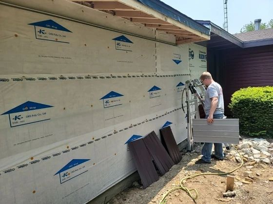 A person installs siding on a house exterior. White weather-resistant barrier covers the wall.