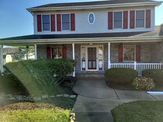 Two-story house with gray siding, red shutters, and a covered porch. A concrete path leads to the front door.