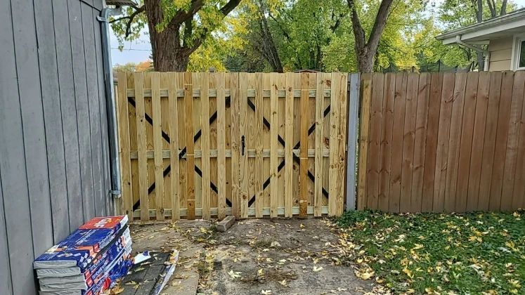 Wooden gate with diamond design and wood fence in a yard, autumn leaves on the ground.