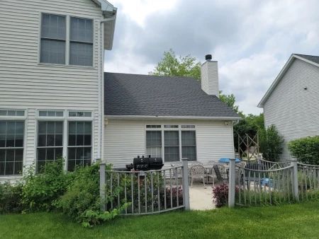 Backyard with a white house, patio, and fence; green grass and bushes.