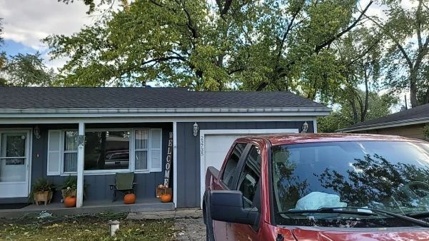 A red truck parked in front of a blue house with a gray roof and fall decorations.
