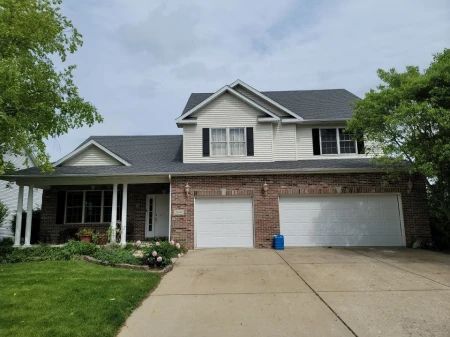 Two-story brick house with a porch, two-car garage, and a driveway, under a cloudy sky.
