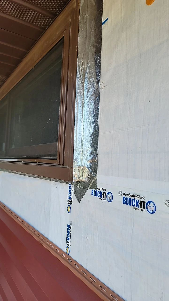 Window frame with flashing installed on a wall with white and red siding.