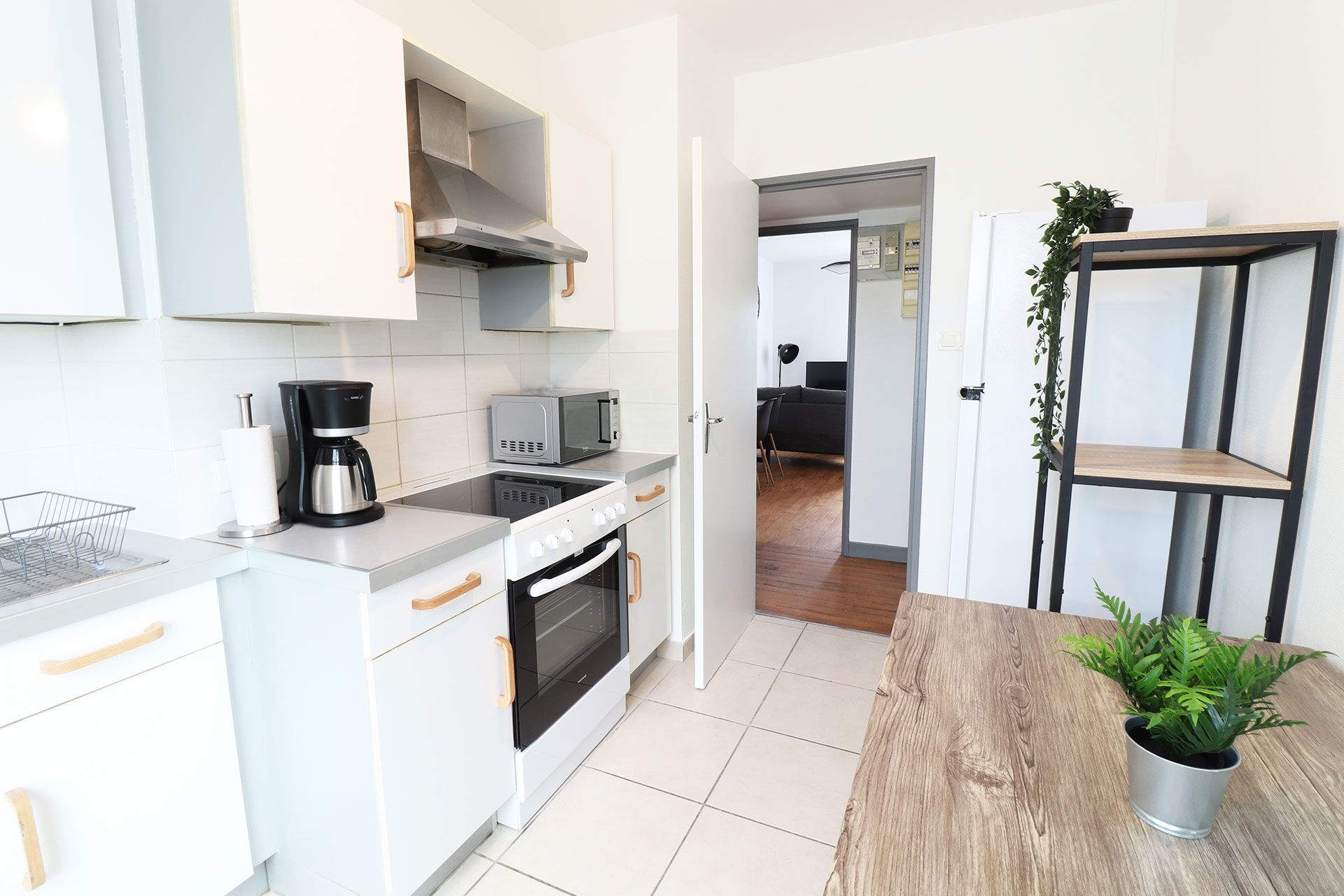 White kitchen with appliances, door to another room, and a wooden table.