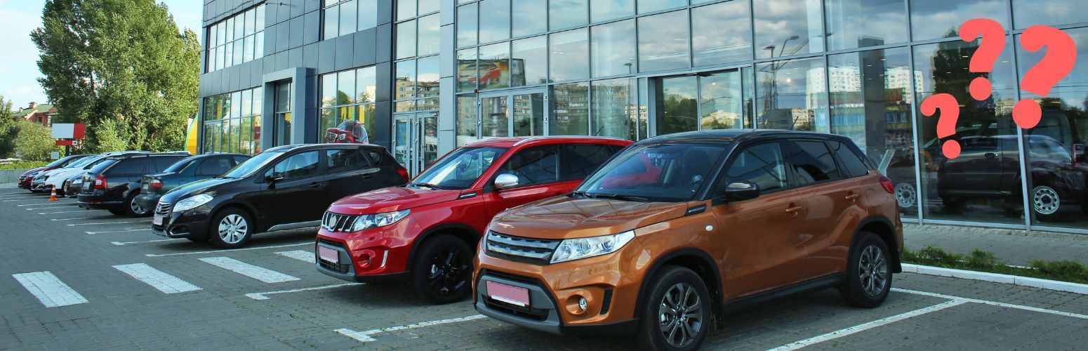 A row of cars are parked in front of a car dealership.